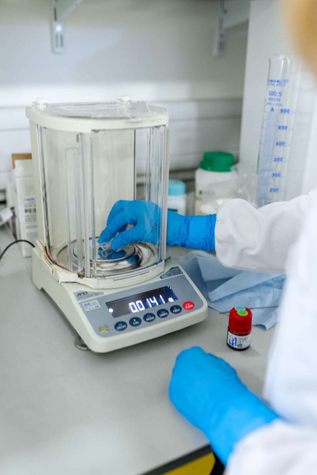 Científico con guantes pesando una muestra líquida en una balanza analítica de precisión