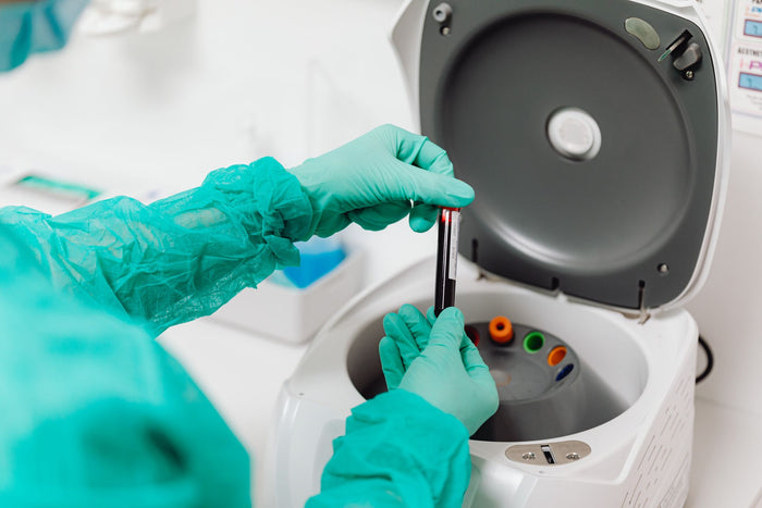 Técnico de laboratorio con guantes introduciendo un tubo de muestra en una centrífuga abierta